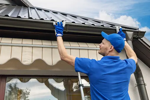 A man in blue shirt and gloves on ladder.